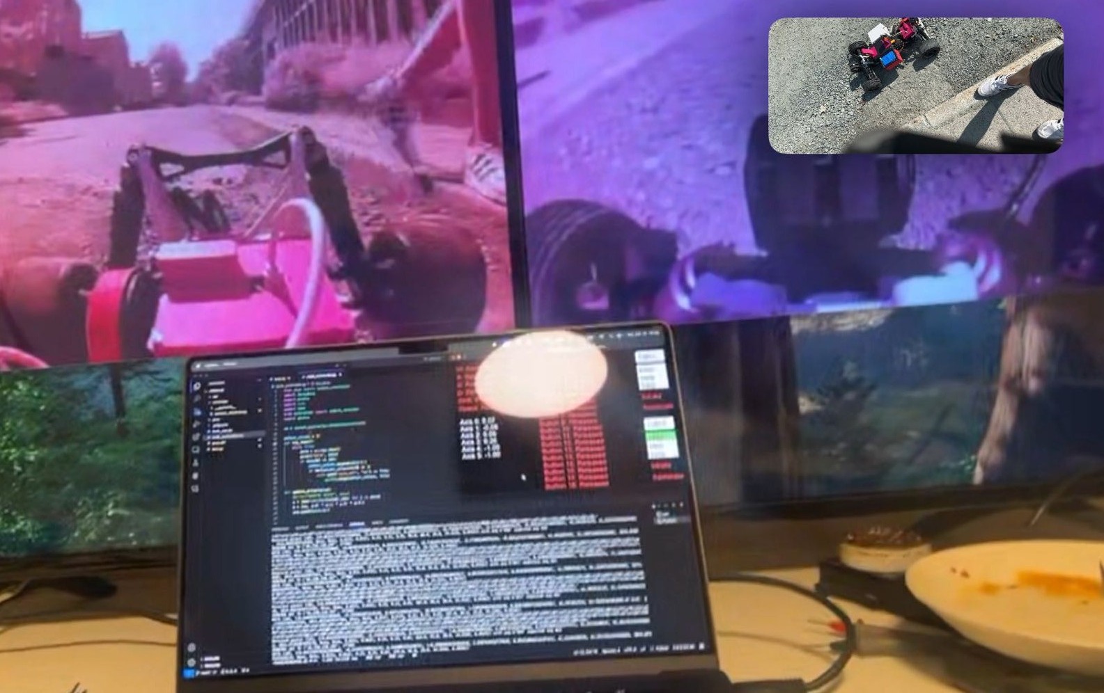 Driving station mid-session: two large monitors above a laptop, each monitor showing one of the car's two cameras (a low forward view down a road and a wider chase view). A picture-in-picture overlay in the corner shows the actual RC car on tarmac next to a person's shoe. The laptop screen is split between code on the left and live telemetry numbers (steering, throttle, axis values) on the right.