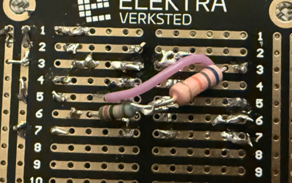 Close-up of a black Elektra Verksted veroboard with a couple of through-hole resistors and a violet wire soldered between pads.